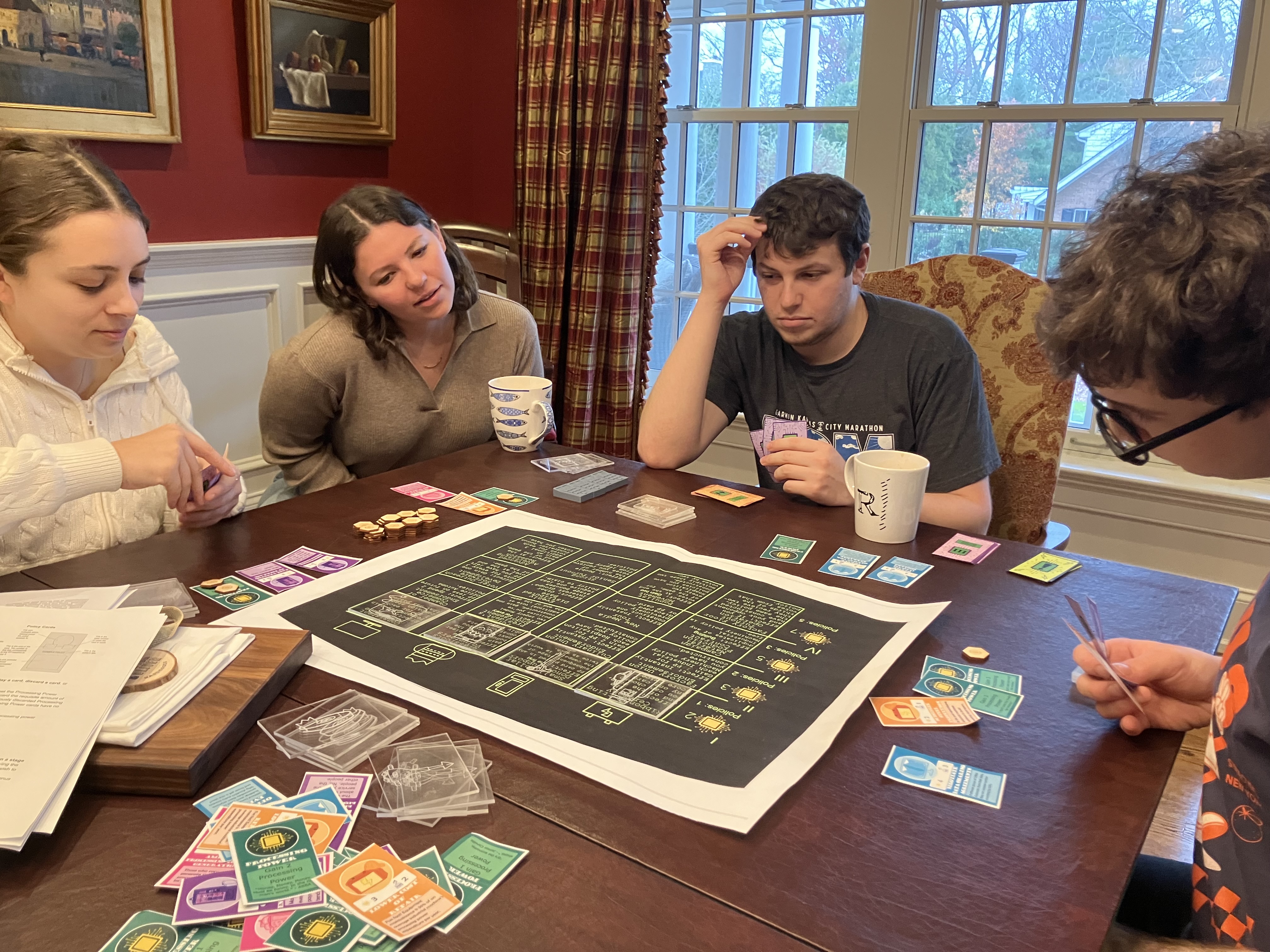 A group of four people sits around a table, engaged in an intense game of Campaign Trail 3000. They look invested and excited.